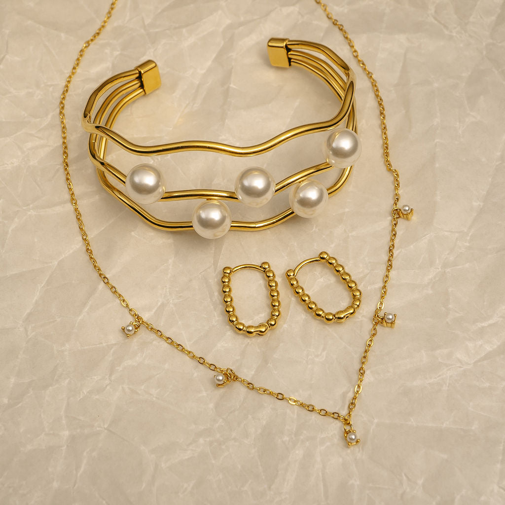 Gold bracelet with pearls and matching earrings on a beige textured background