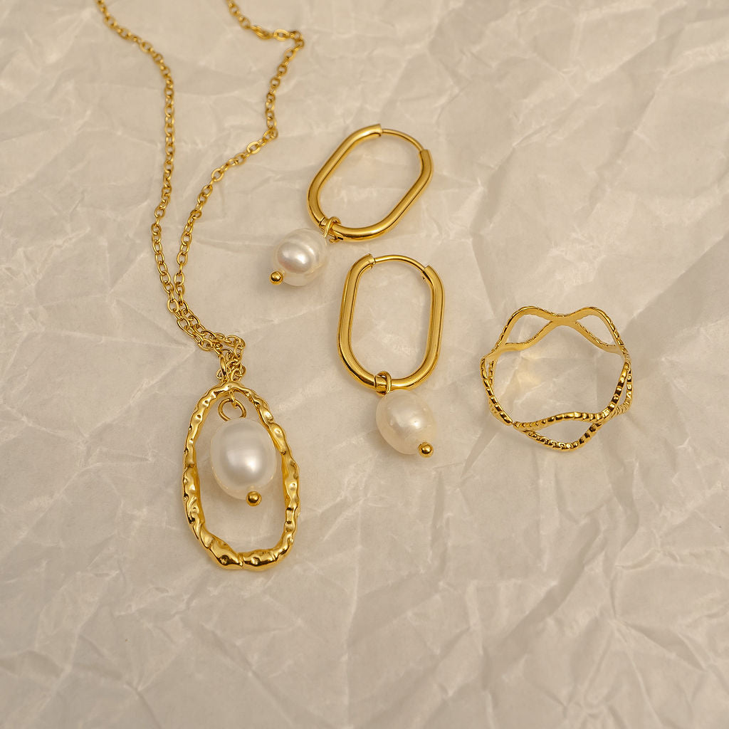 Gold jewelry set with pearls on a textured beige surface