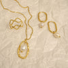 Gold jewelry set with necklaces and earrings on a textured beige background