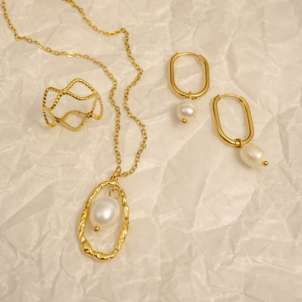 Gold jewelry set with necklaces and earrings on a textured beige background