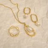 Gold jewelry set with pearls on a textured beige background
