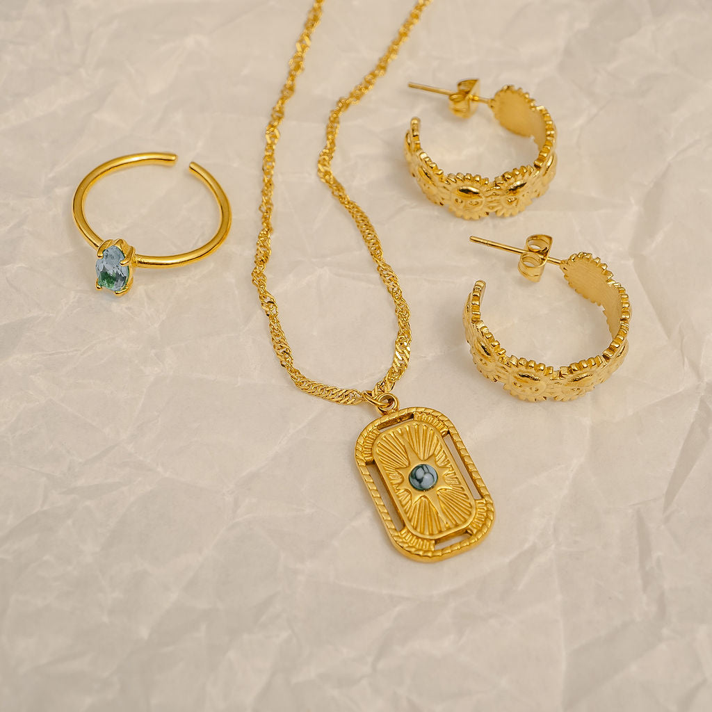 Gold jewelry set with necklace and hoop earrings on a beige textured background