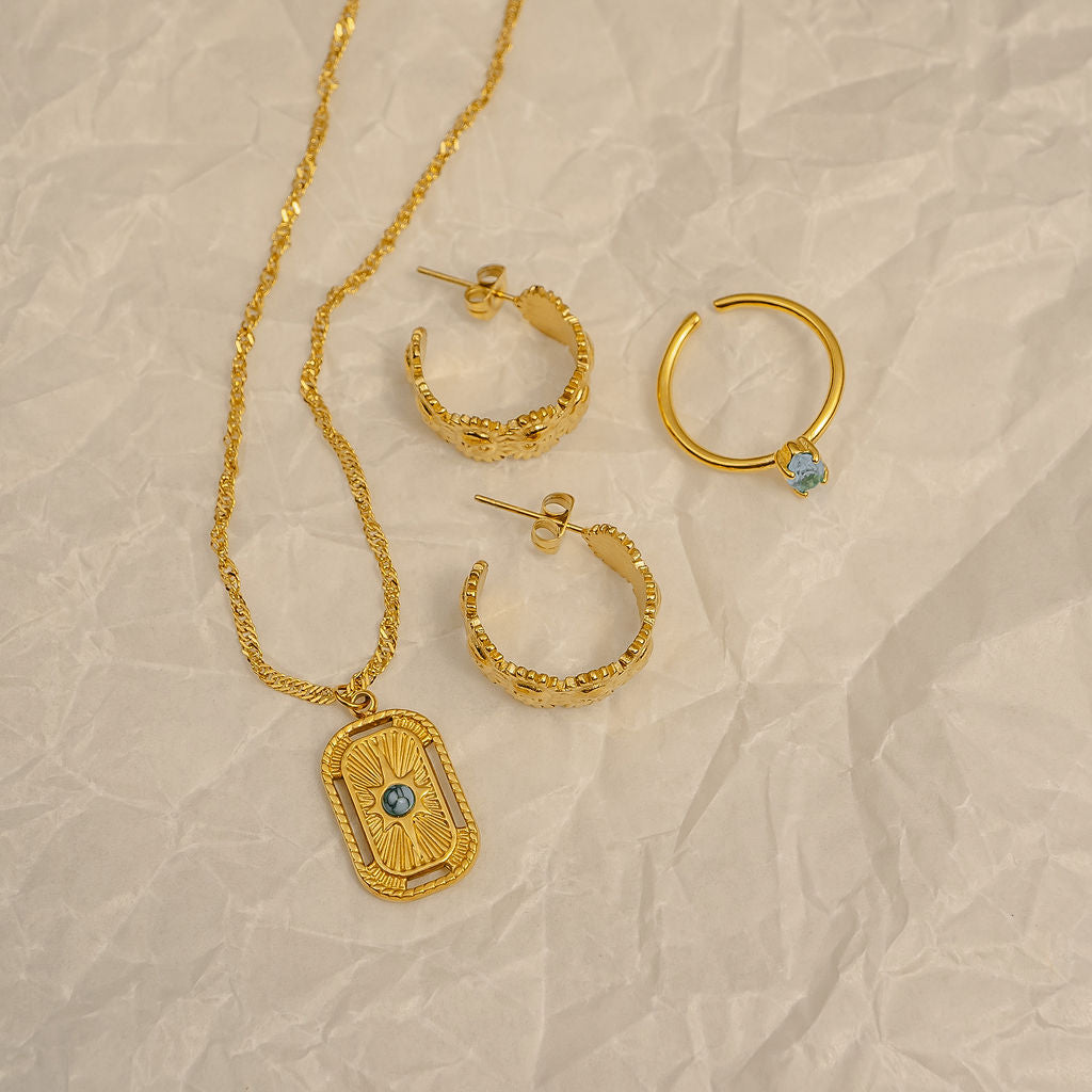 Gold necklace and hoop earrings with gemstones on a beige textured background