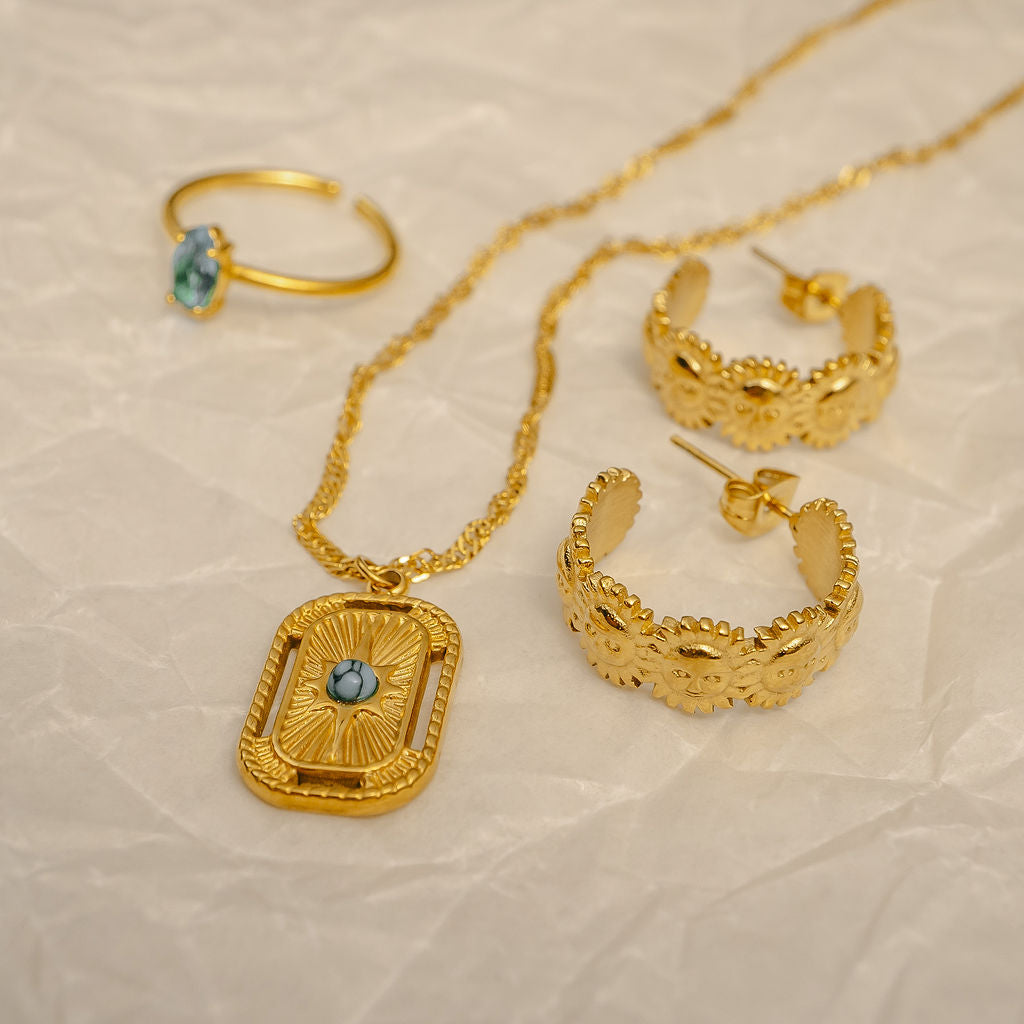 Gold jewelry set including necklace, hoop earrings, and ring on a beige background
