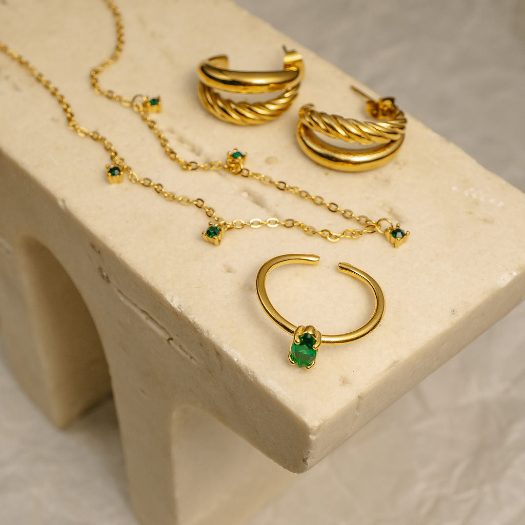 Gold jewelry set with necklaces and earrings on a beige stone surface