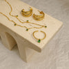 Gold jewelry set with emerald stones on a beige stand
