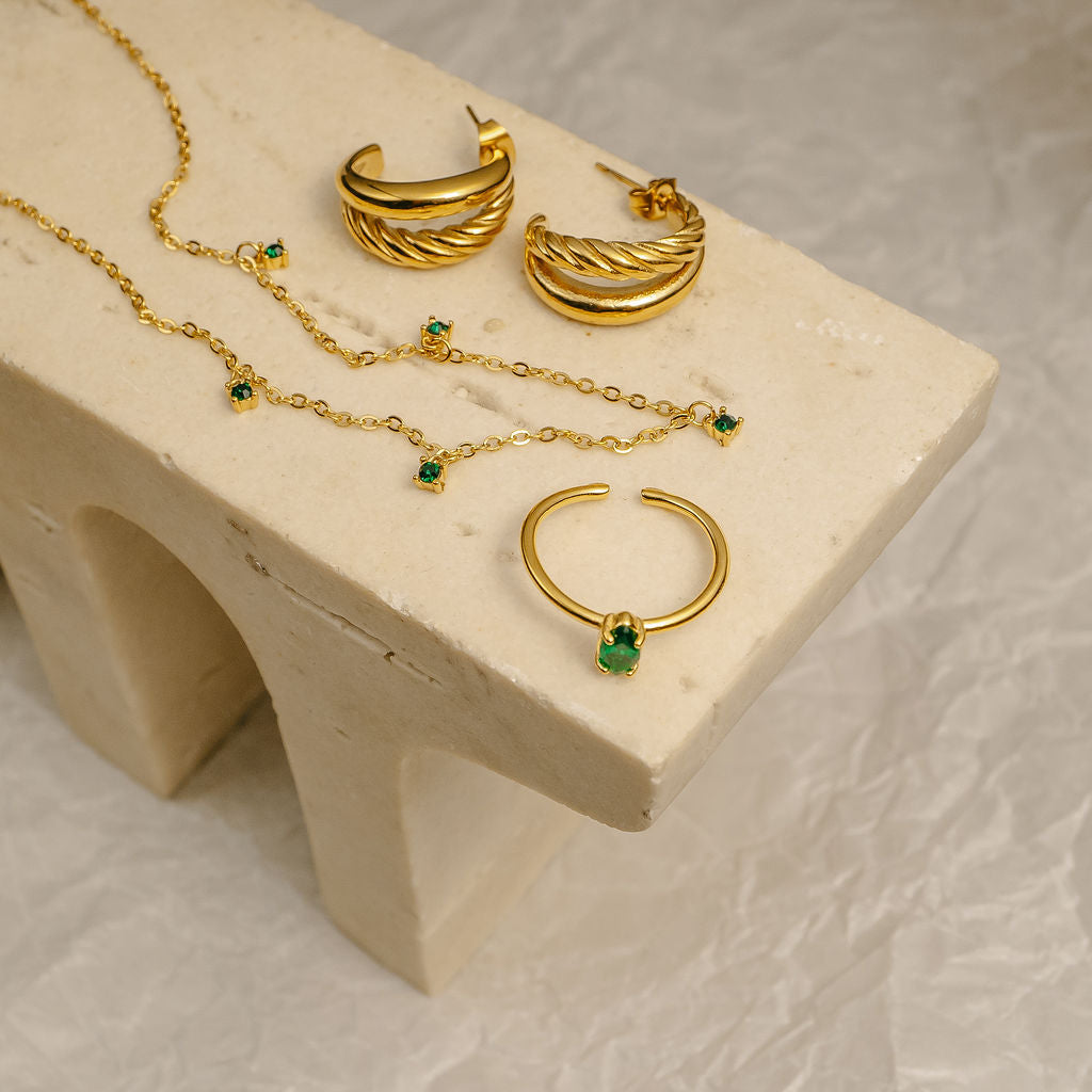 Gold jewelry set with emerald stones on a beige stand