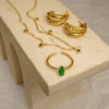 Gold jewelry set with emerald stones on a beige stand