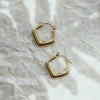 A pair of gold-colored hoop earrings on a crumpled silver paper background