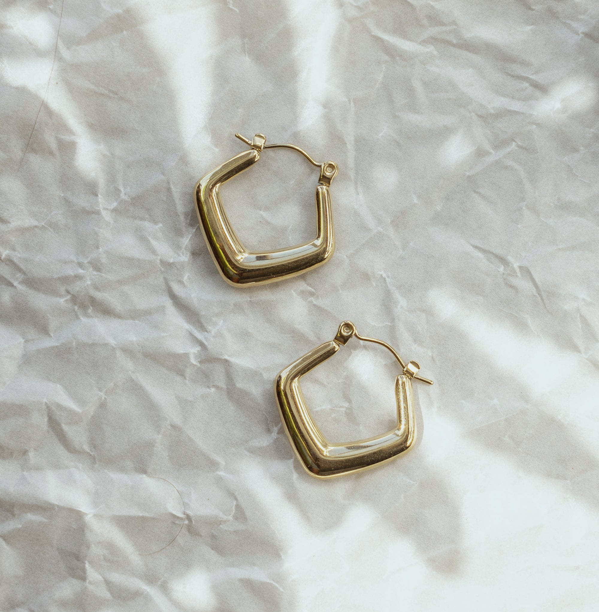 A pair of gold-colored hoop earrings on a crumpled silver paper background