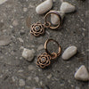 Rose gold hoop earrings with gemstones on a textured surface with stones.