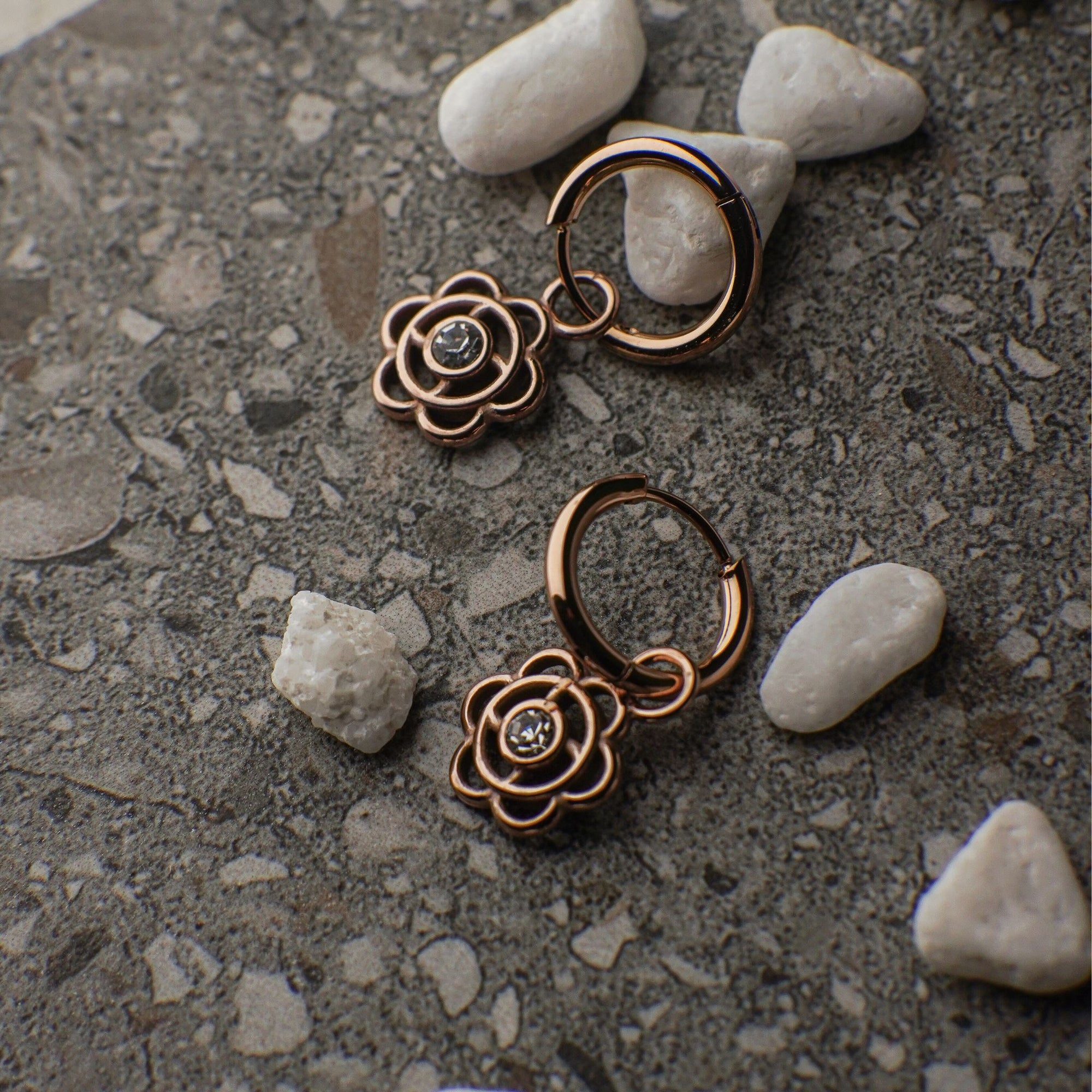Rose gold hoop earrings with gemstones on a textured surface with stones.
