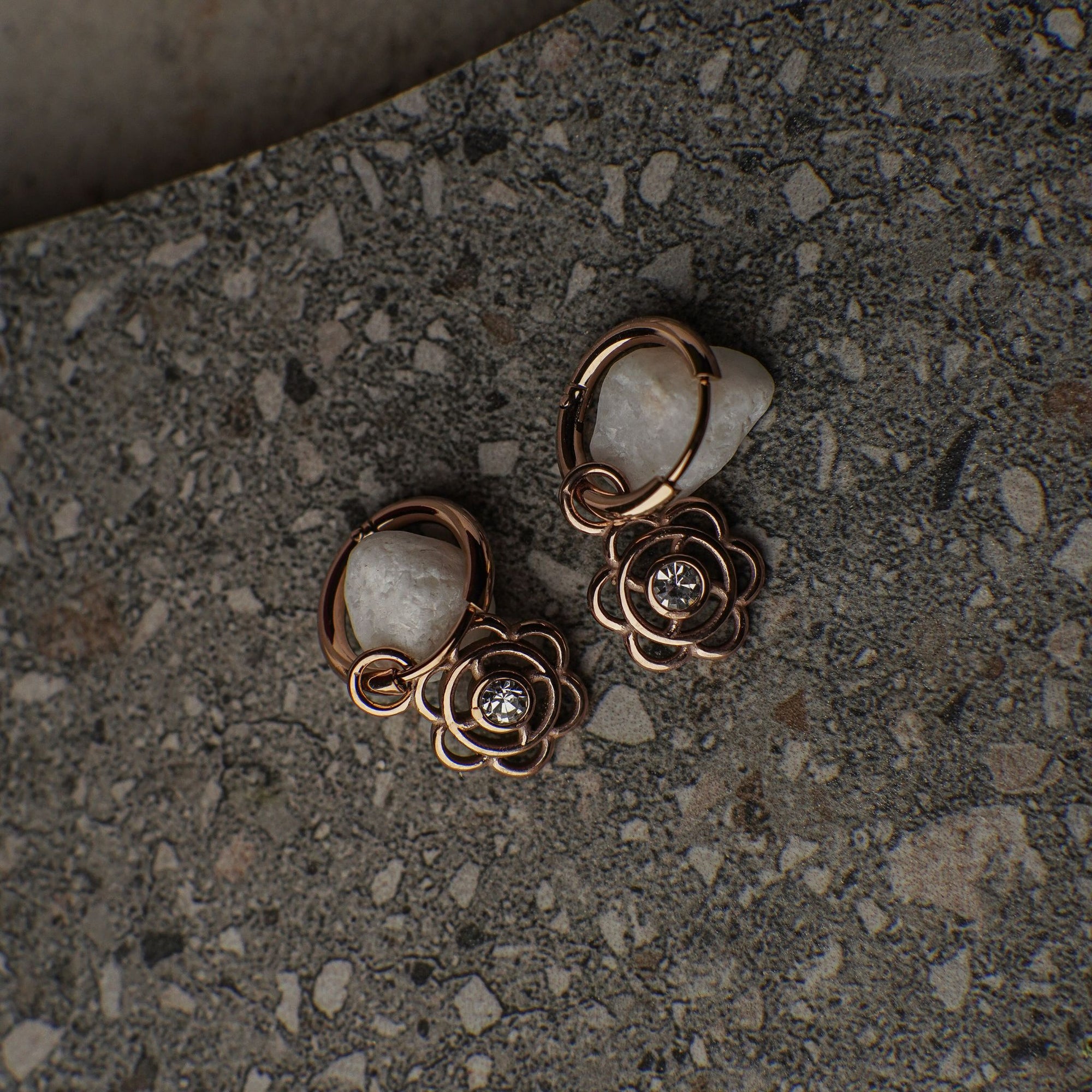 Pair of rose gold floral earrings on a textured surface