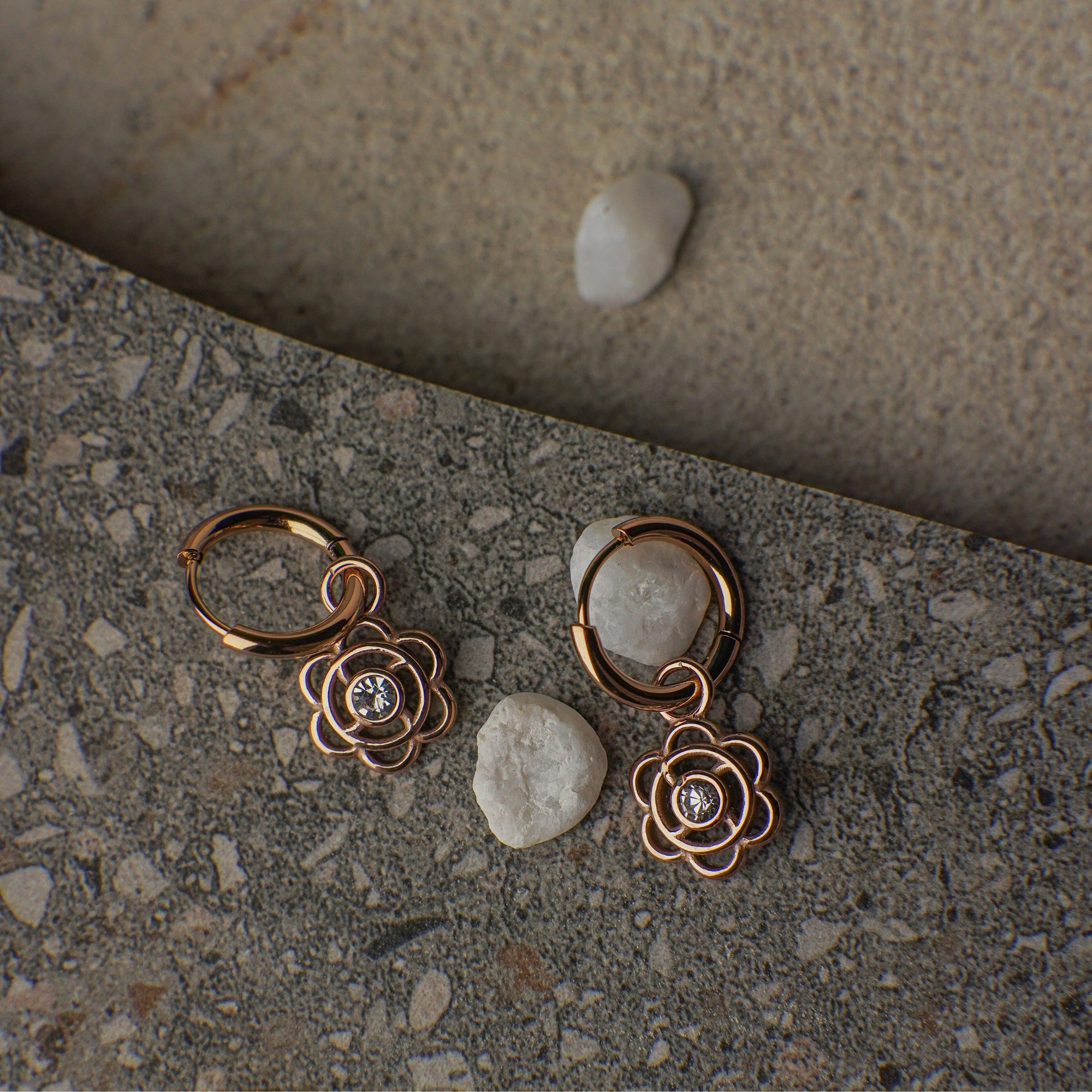 Pair of rose gold floral earrings on a stone surface