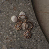 Pair of rose gold floral earrings with small stones on a textured surface