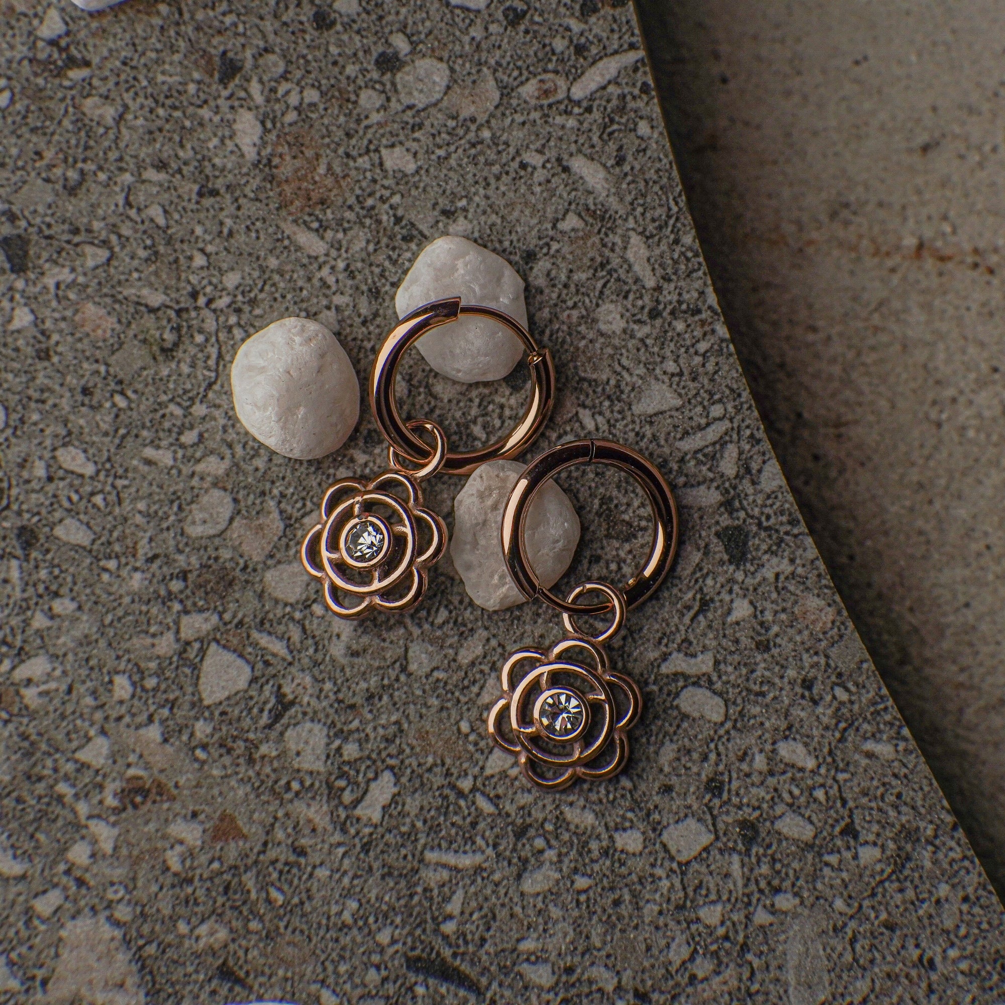 Pair of rose gold floral earrings with small stones on a textured surface