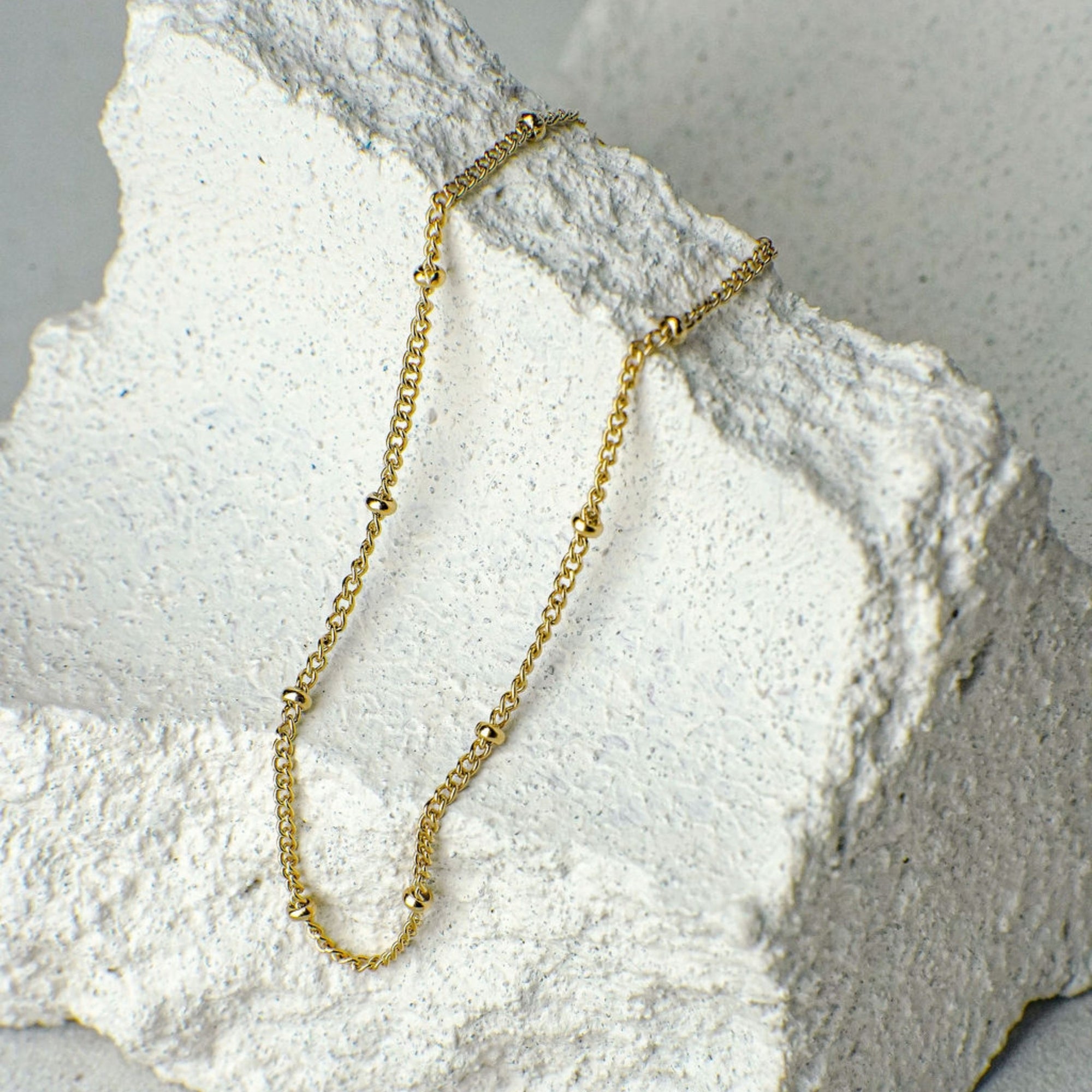 Gold chain necklace on a textured white surface