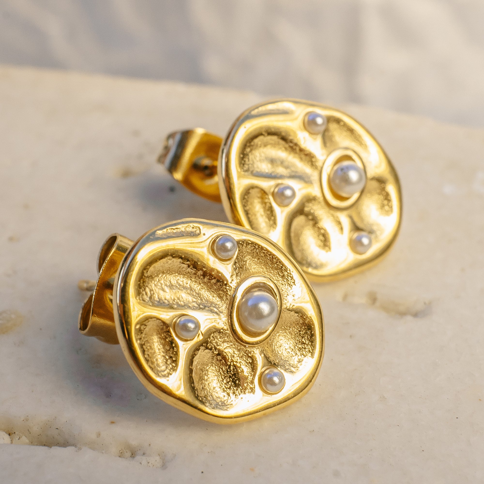 Gold earrings with pearl-like stones on a beige surface