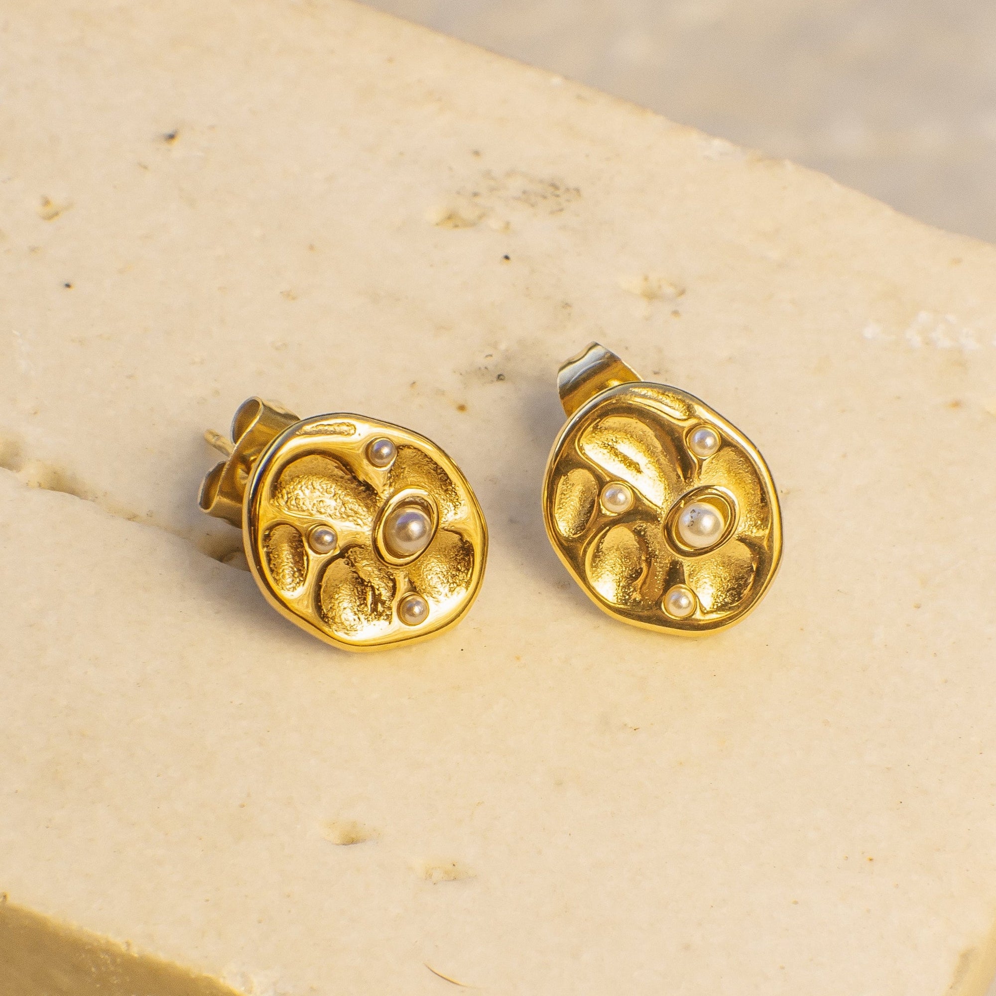 Gold earrings with a central pearl on a beige stand.