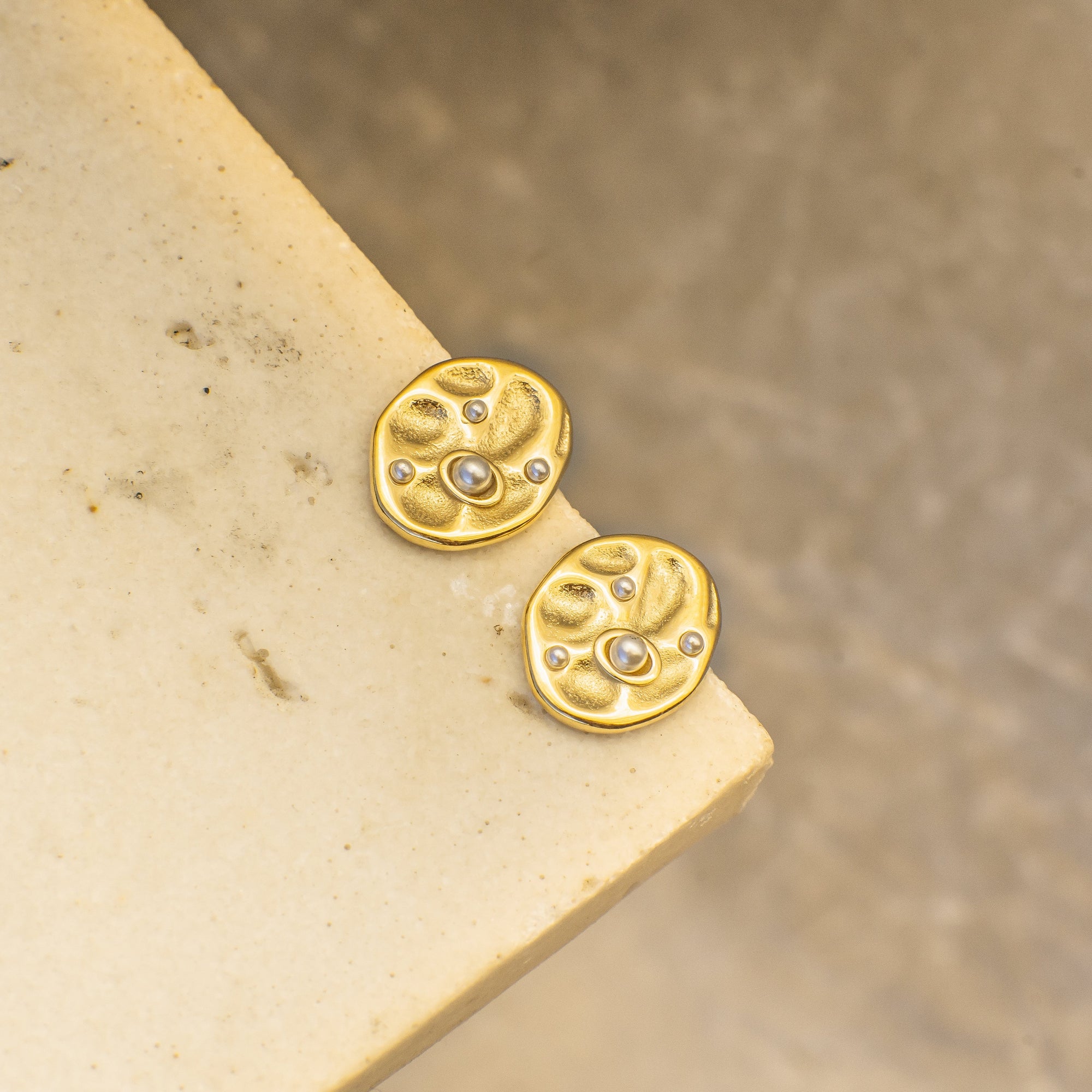 Gold earrings with circular design on a beige surface