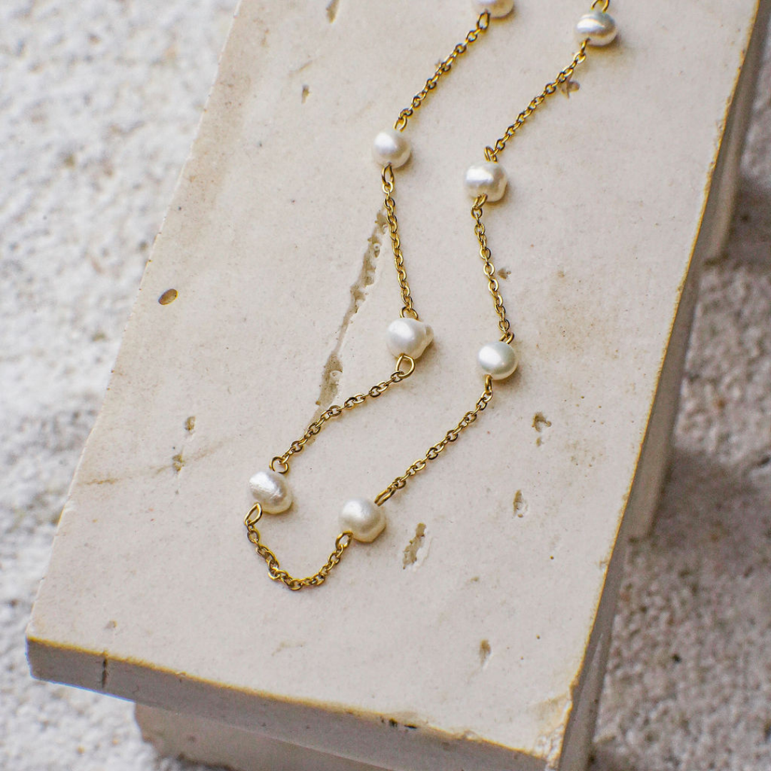 Gold chain necklace with pearls on a textured surface