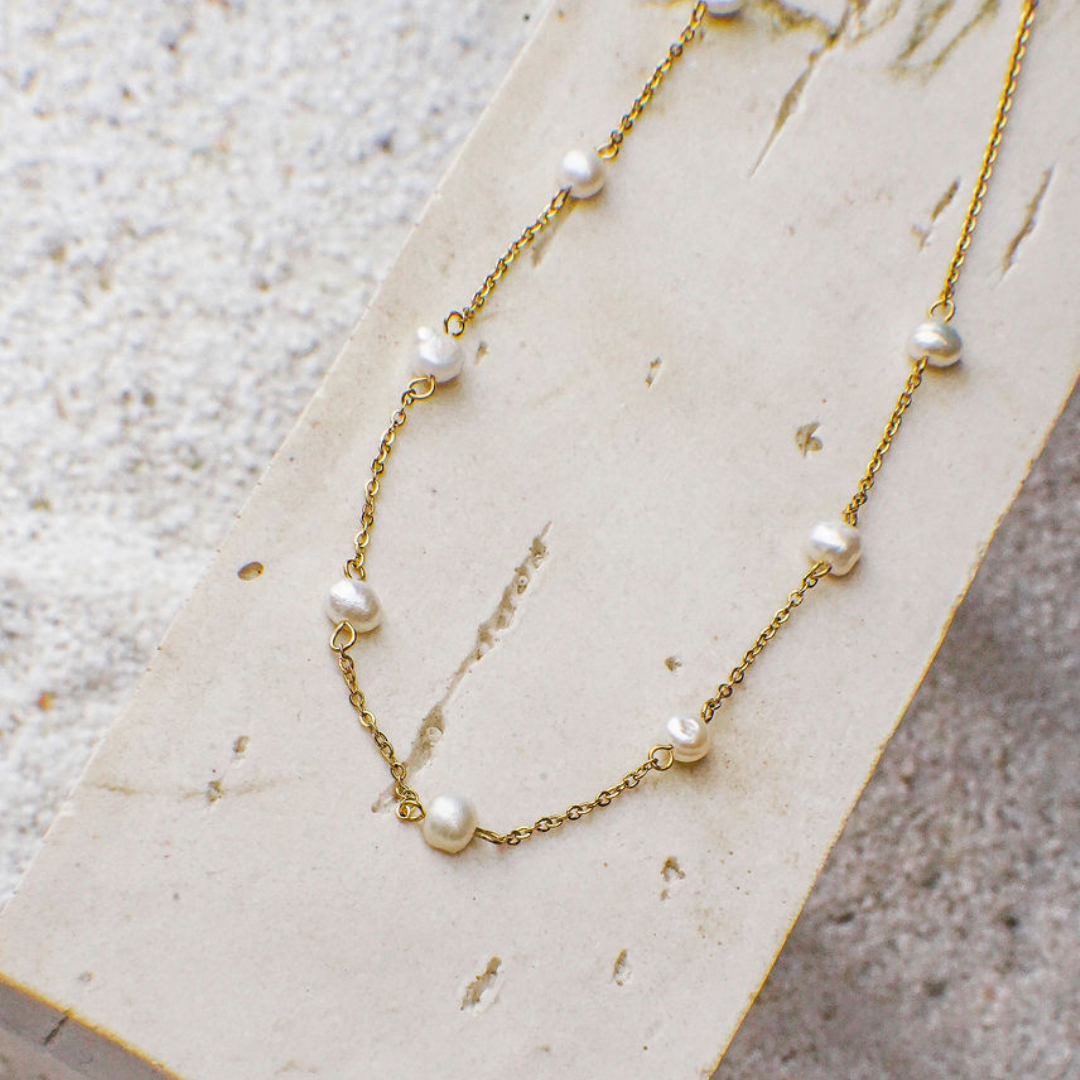 Gold necklace with pearls on a textured beige surface