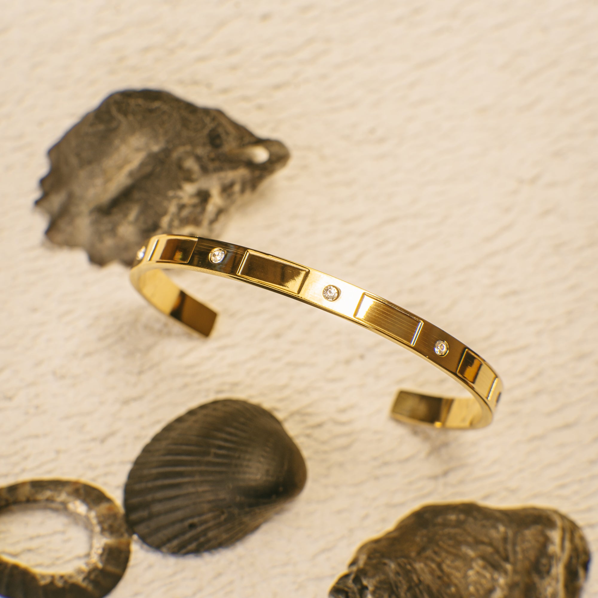 Gold bracelet with embedded stones on a textured beige background