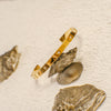 Gold bracelet on a textured beige surface with seashells