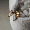 Gold earrings with clear gemstones on a textured white surface