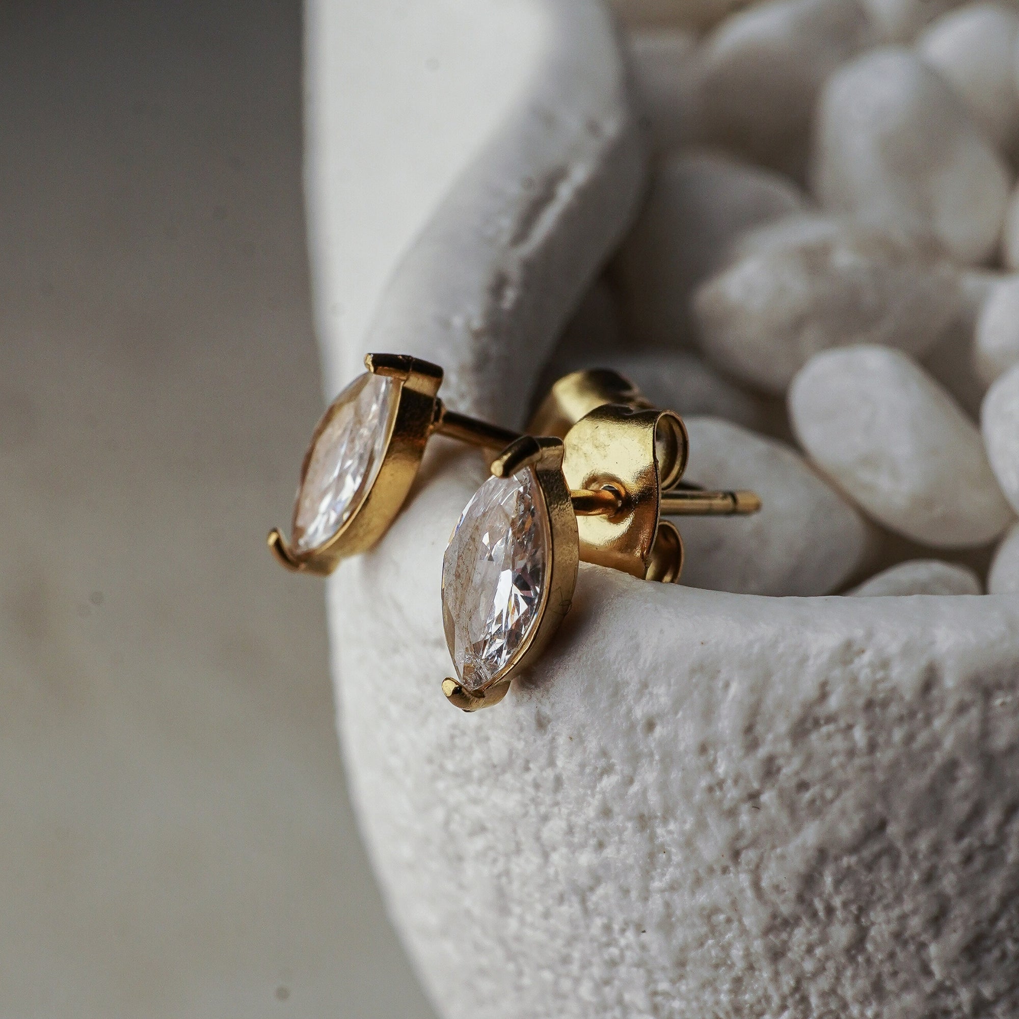Gold earrings with clear gemstones on a textured white surface