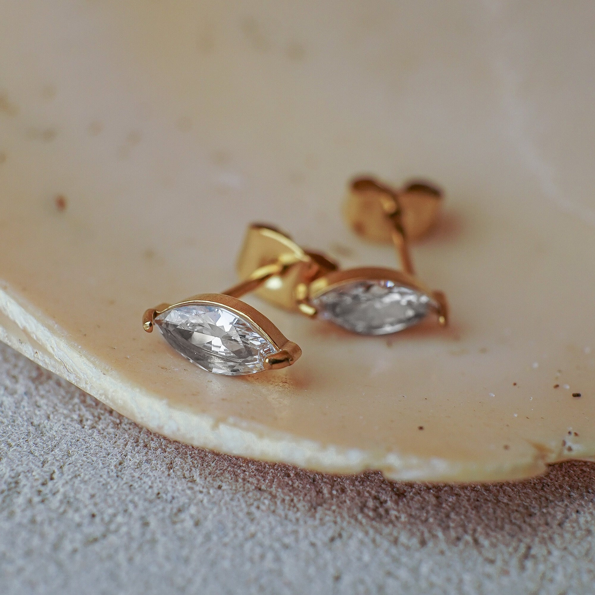 Gold earrings with clear gemstones on a beige shell