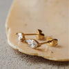 Gold earrings with clear gemstones on a beige stone surface