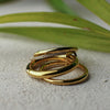 Three gold rings stacked on a textured surface with green leaves in the background