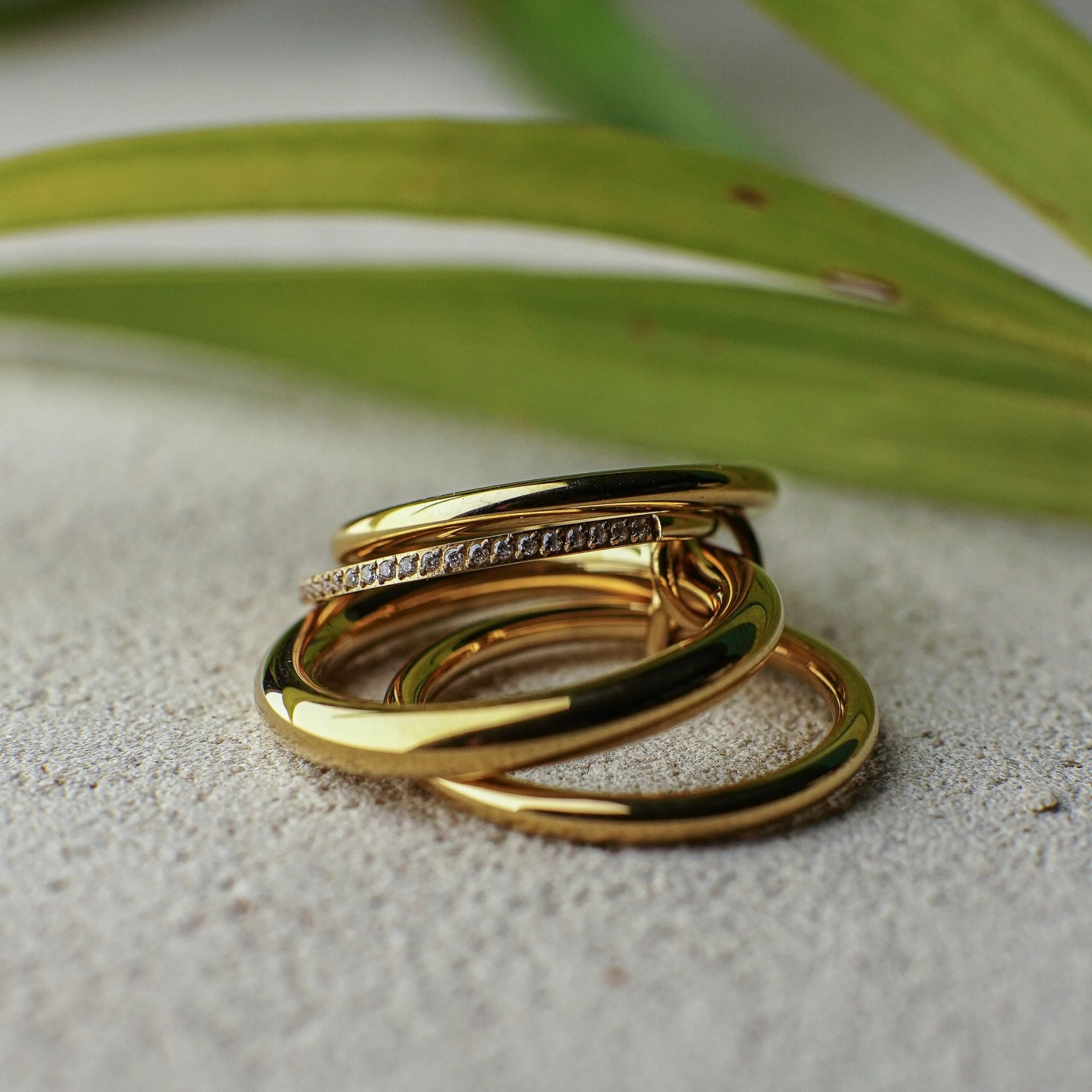 Three gold rings stacked on a textured surface with green leaves in the background