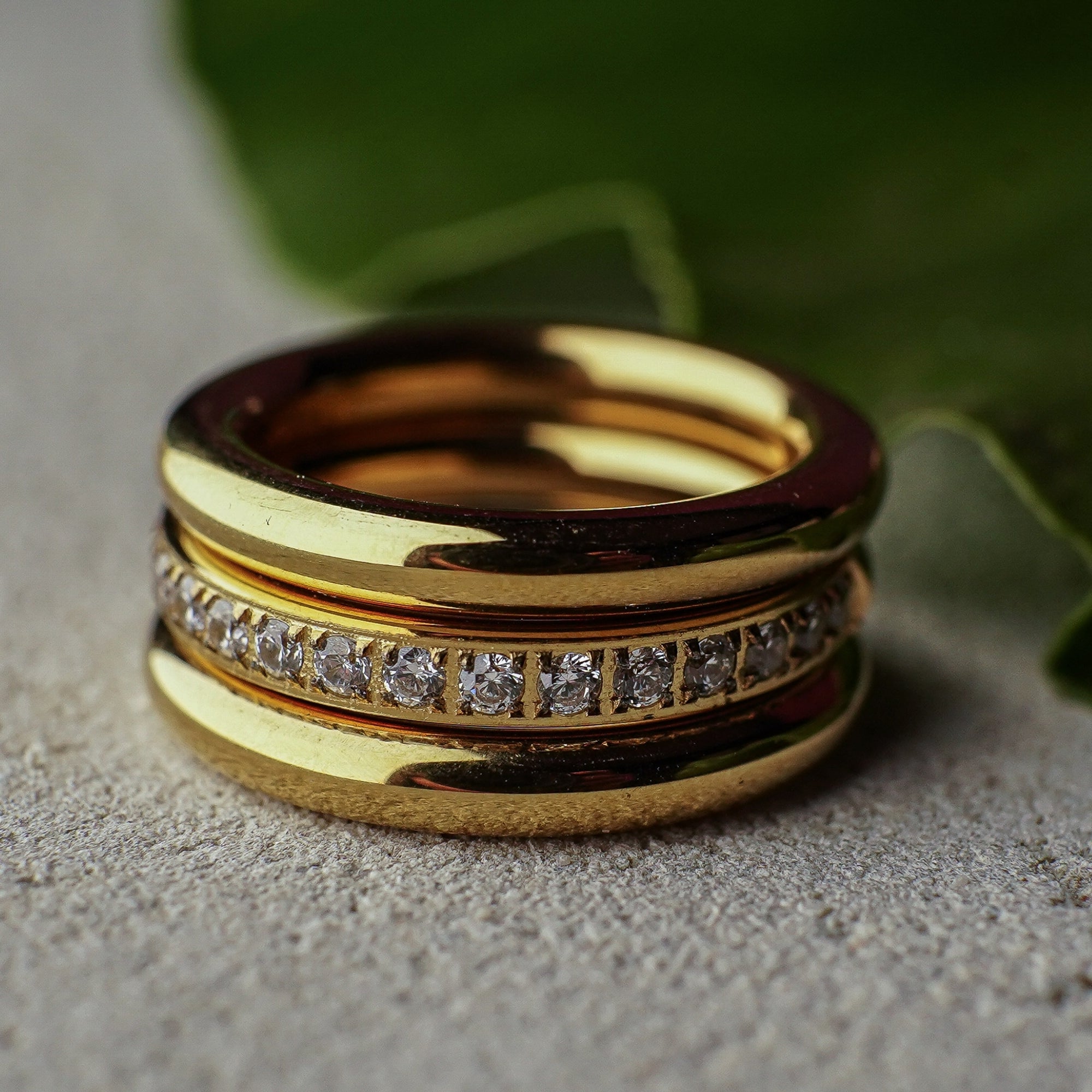 Stack of gold rings with diamond accents on a textured surface with green leaves in the background