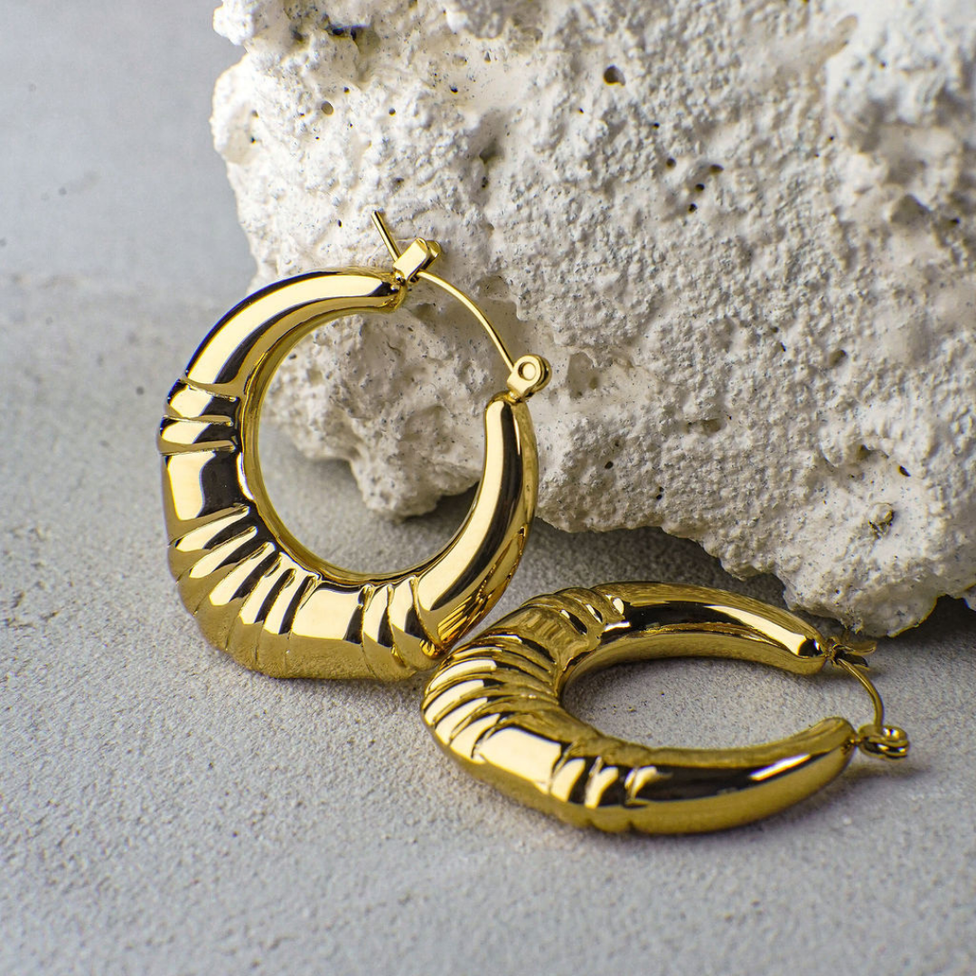 Gold hoop earrings on a textured stone surface