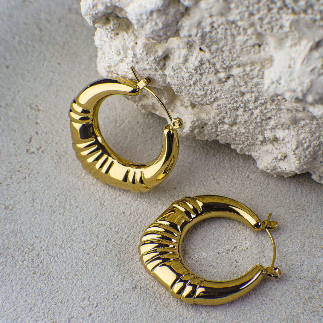 Gold hoop earrings on a textured stone surface