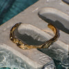 Gold bracelet on a stone surface with water in the background