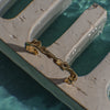 Curvy gold bracelet on a stone surface with water in the background