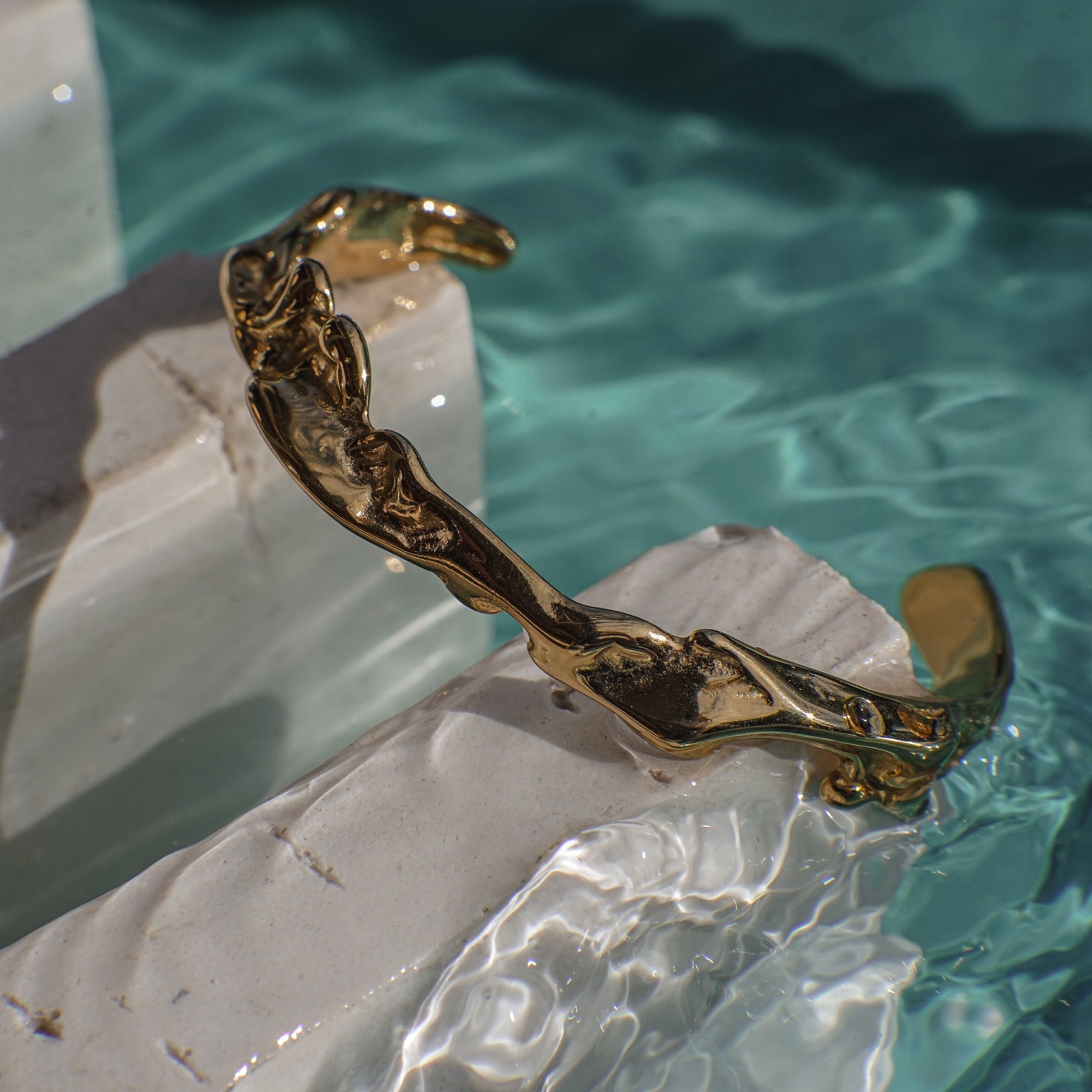 Wavy gold bracelet on a rock with water in the background