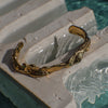 Curvy gold bracelet on a stone ledge with water in the background