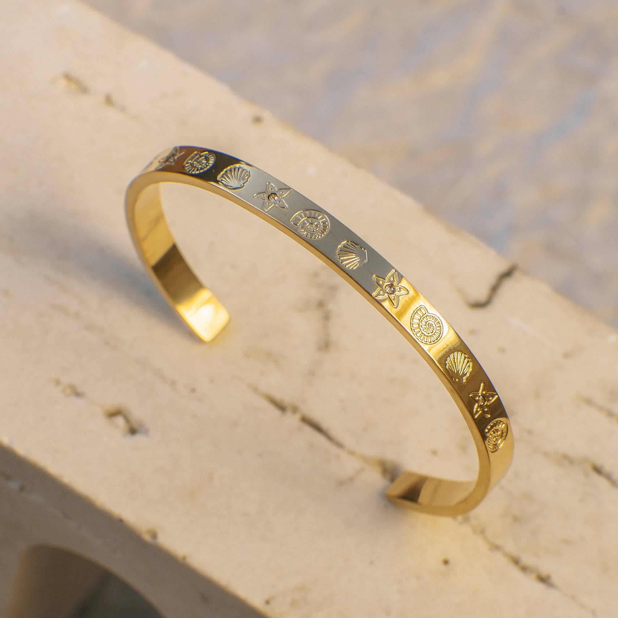 Gold bracelet with engraved ocean creature designs on a textured surface