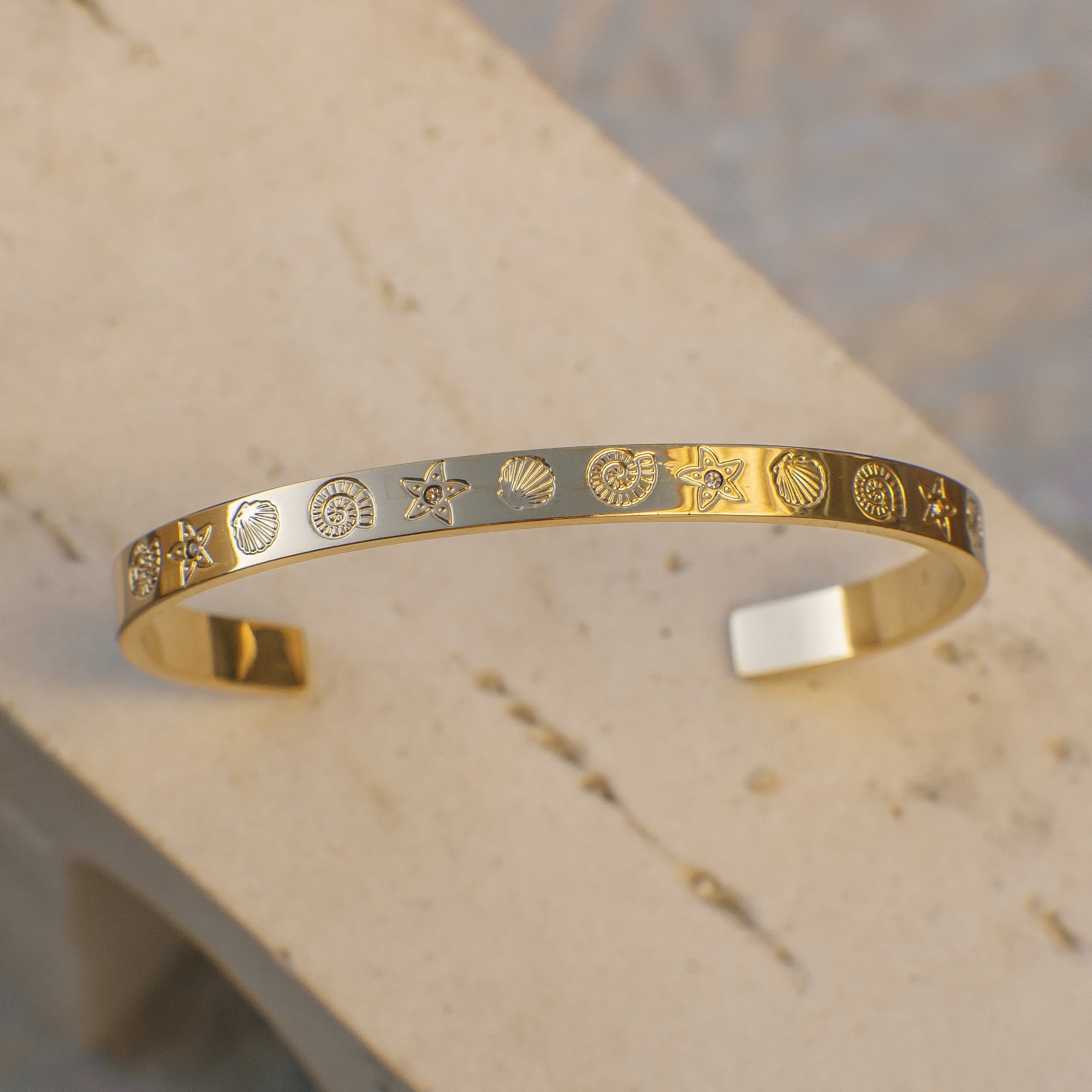Gold bracelet with engraved ocean creature patterns on a beige surface