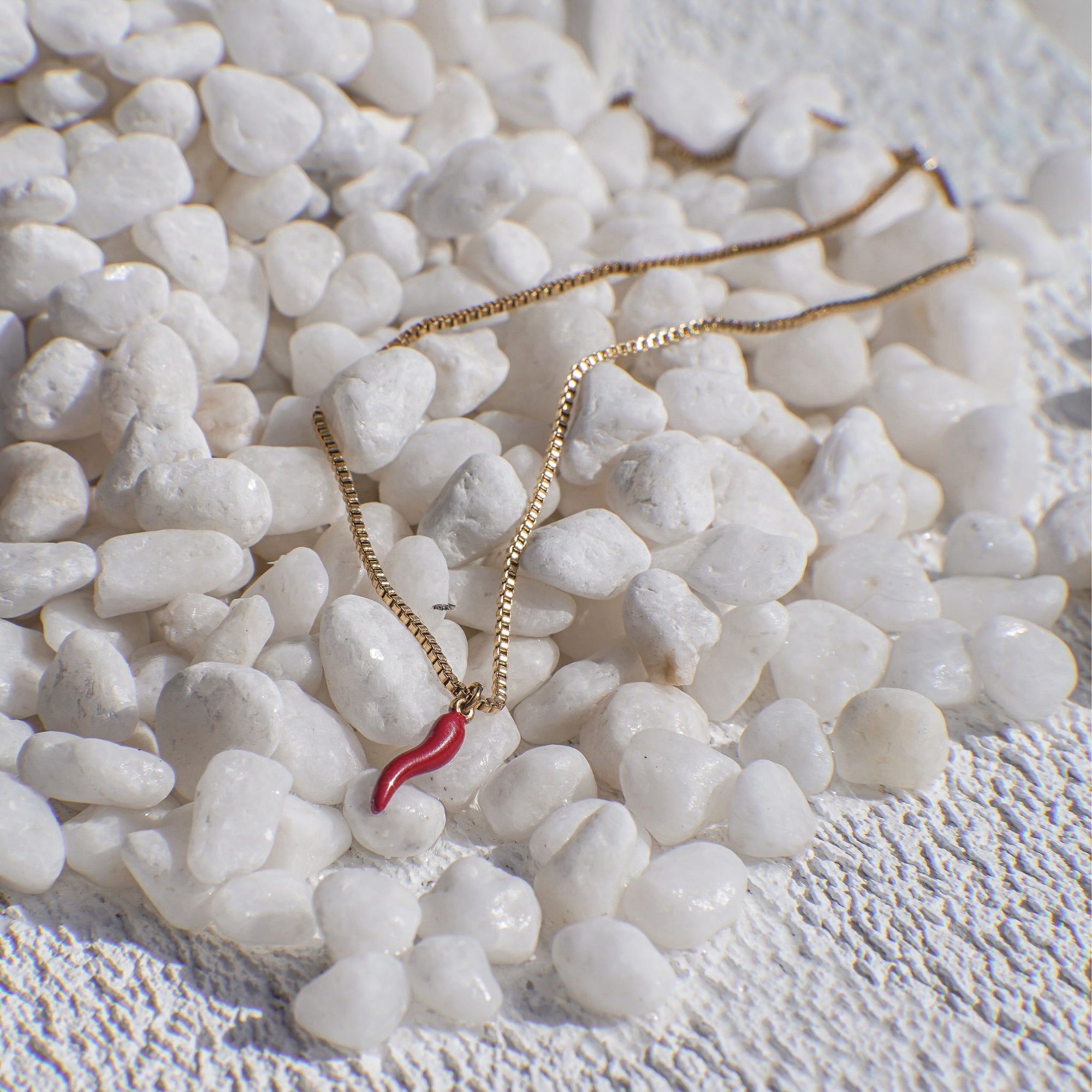 Gold necklace with a red chili pendant on white pebbles