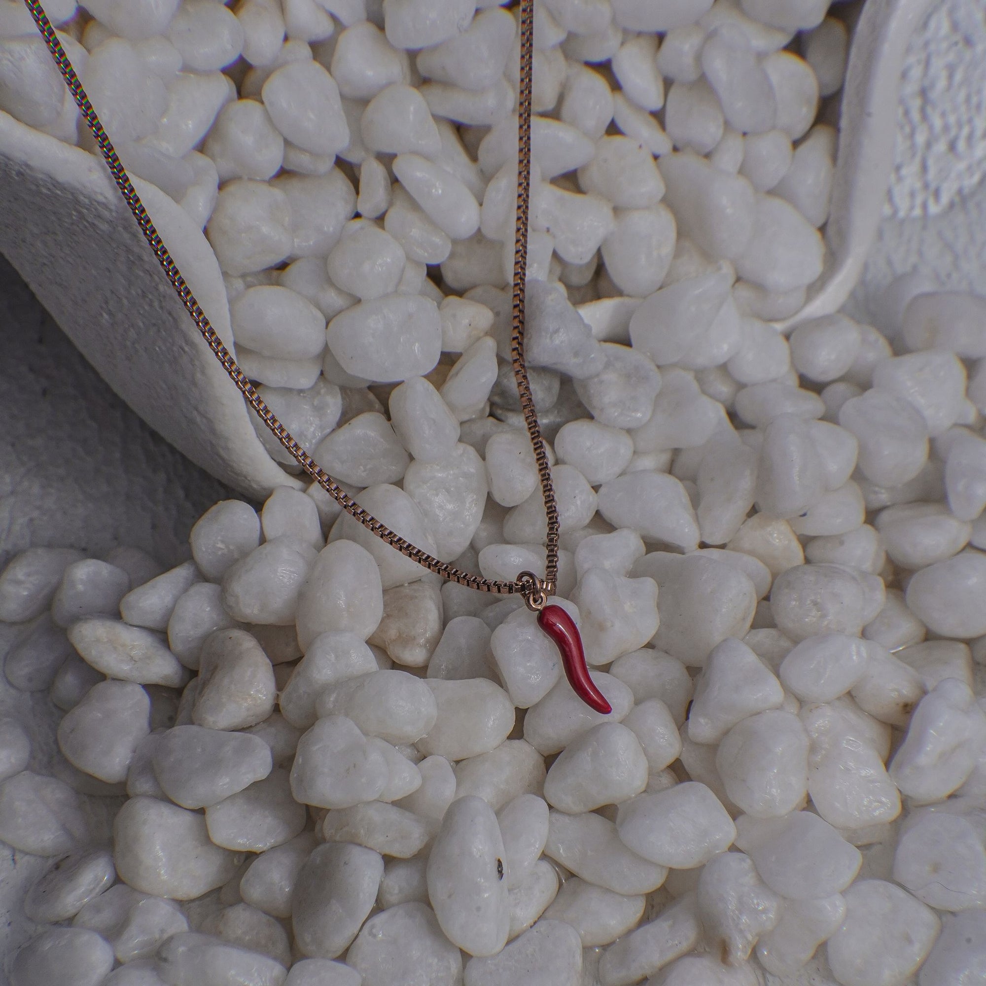 Necklace with a red chili pendant on pebbles