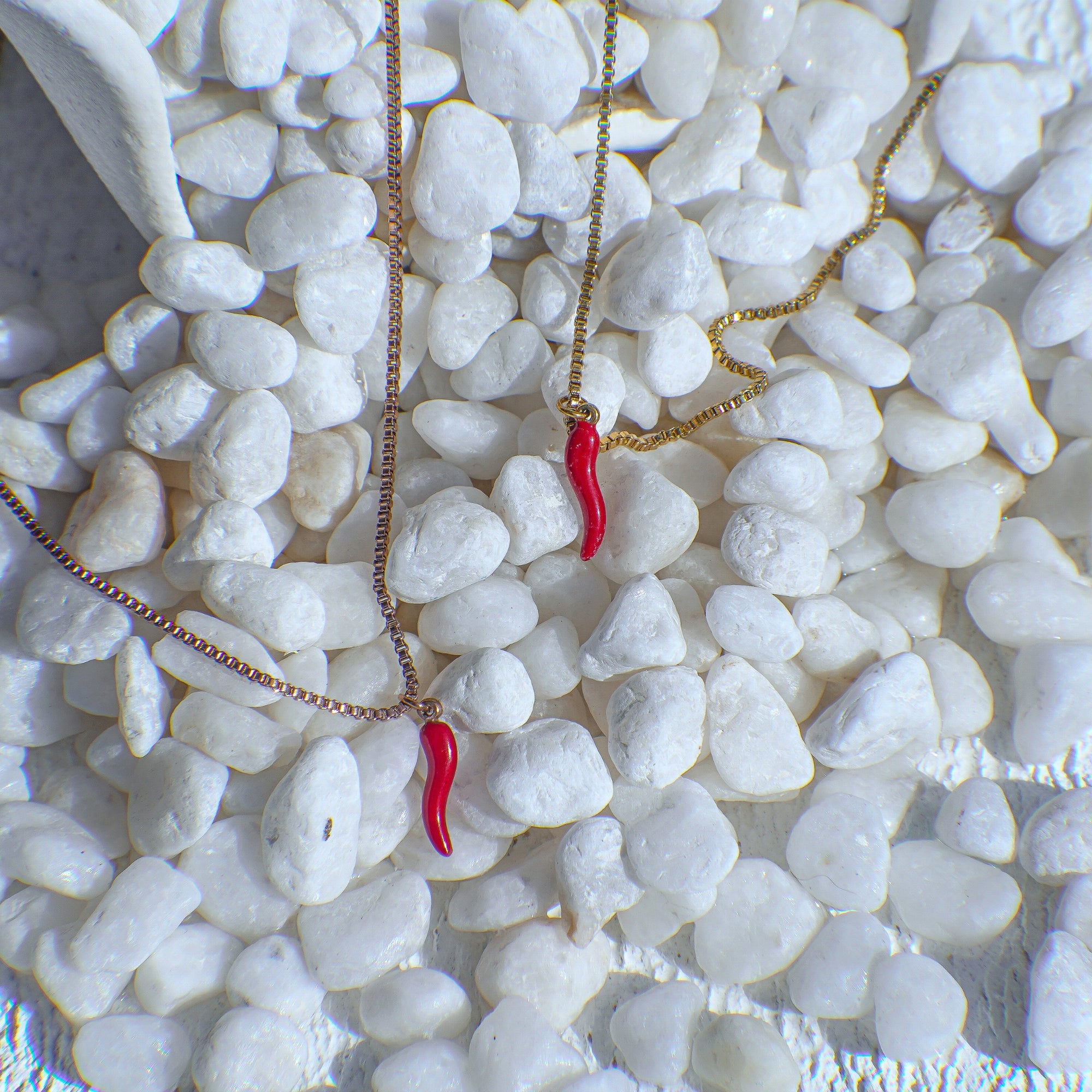 Two necklaces with red chili pendants on a bed of white pebbles.
