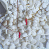 Two necklaces with red chili pendants on a bed of white pebbles