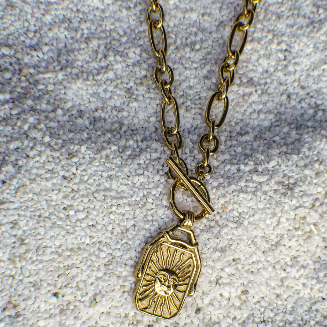 Gold necklace with a pendant on a textured gray surface