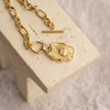 Gold necklace with a lock-shaped pendant on a beige stand.