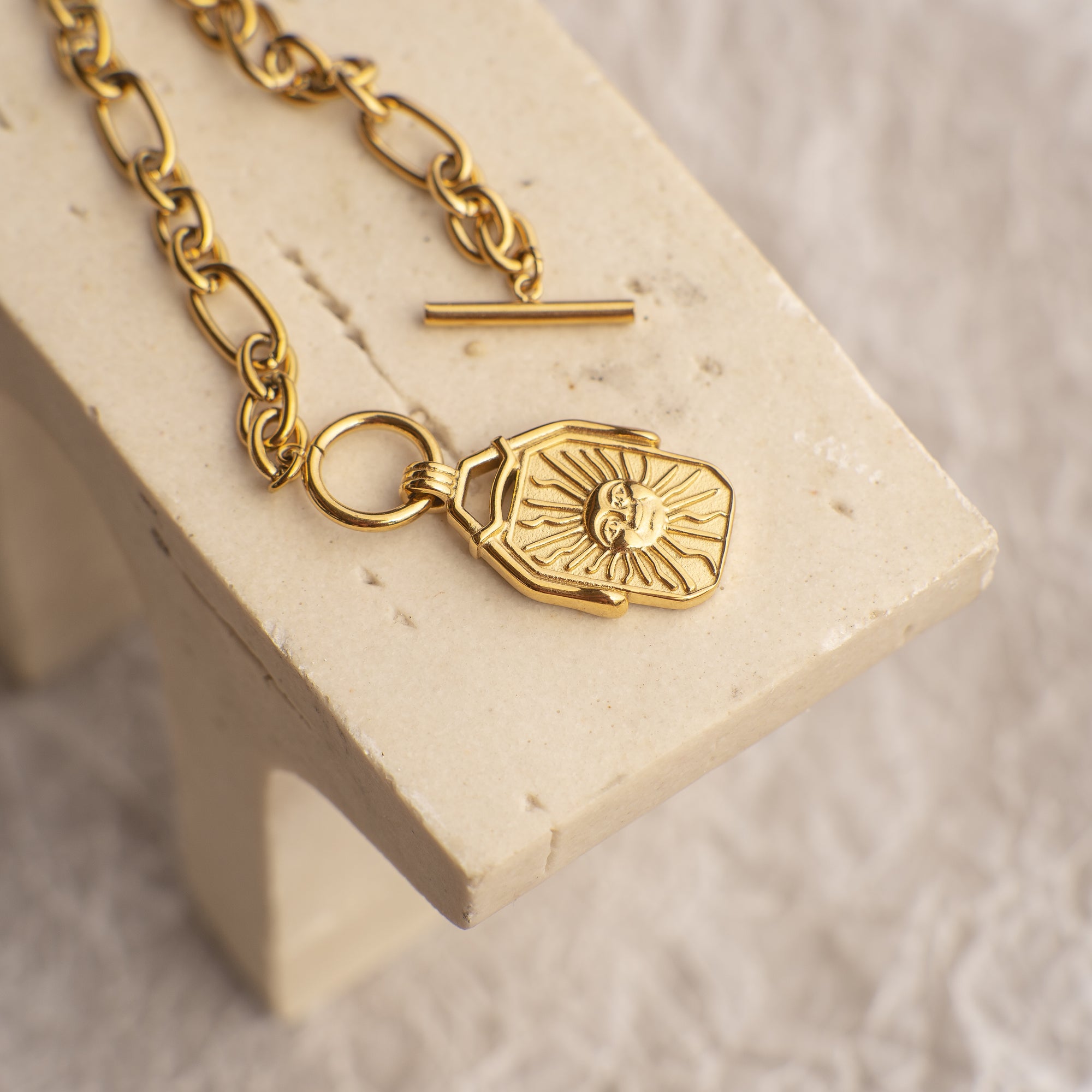 Gold necklace with a lock-shaped pendant on a beige stand.